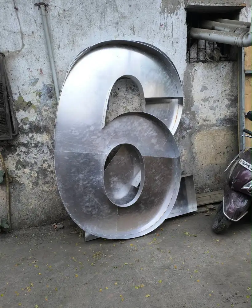 Giant fabricated stainless steel number 6 standing against a workshop wall